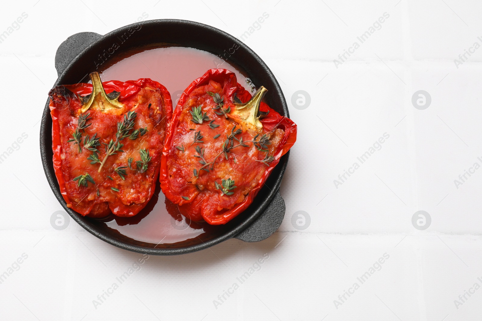 Photo of Tasty stuffed peppers in dish on white tiled table, top view. Space for text