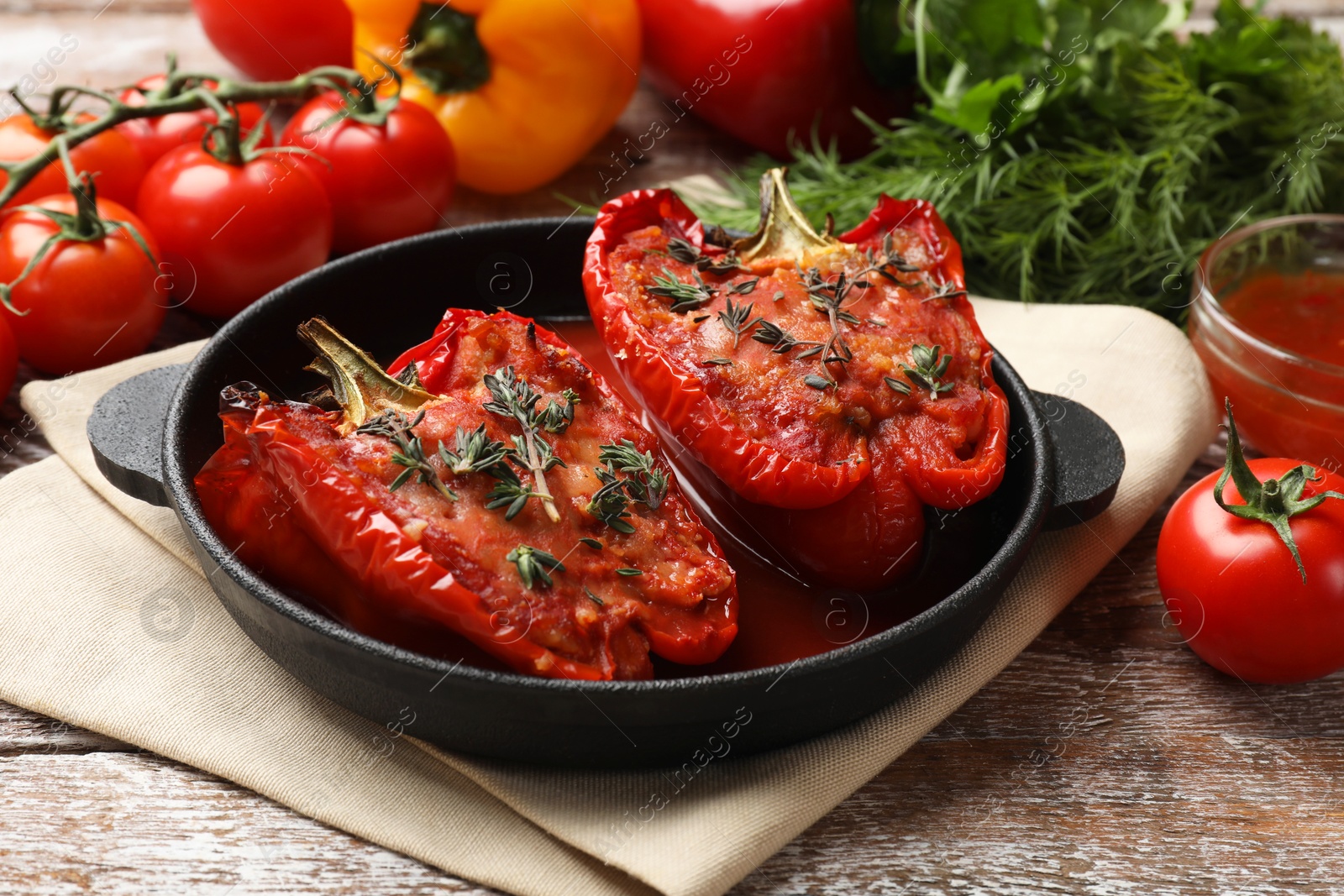 Photo of Tasty stuffed peppers in dish and ingredients on wooden table