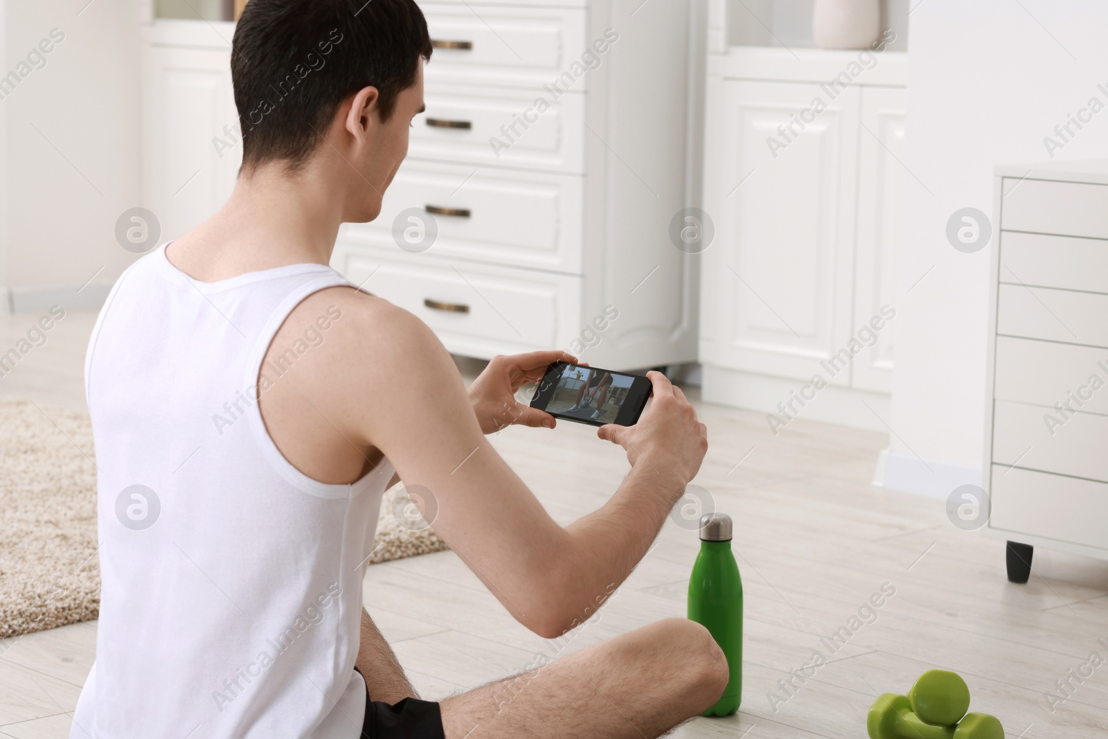 Photo of Online fitness trainer. Man watching tutorial on smartphone at home