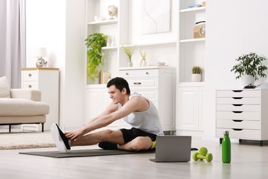 Photo of Online fitness trainer. Man doing exercise near laptop at home