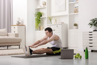 Online fitness trainer. Man doing exercise near laptop at home