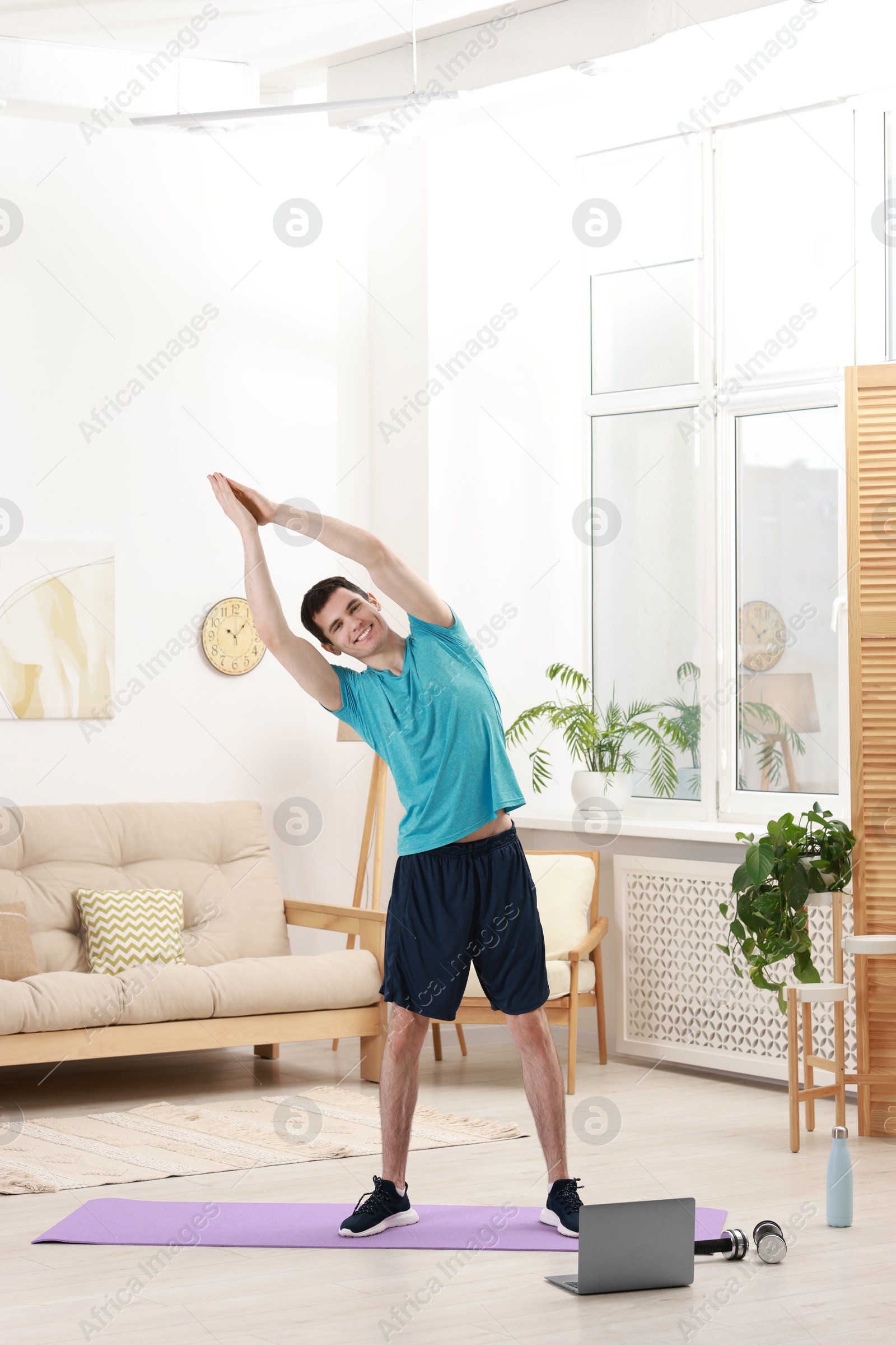 Photo of Online fitness trainer. Man doing exercise near laptop at home