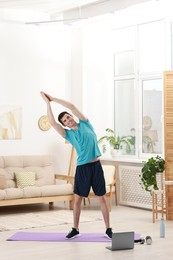 Online fitness trainer. Man doing exercise near laptop at home