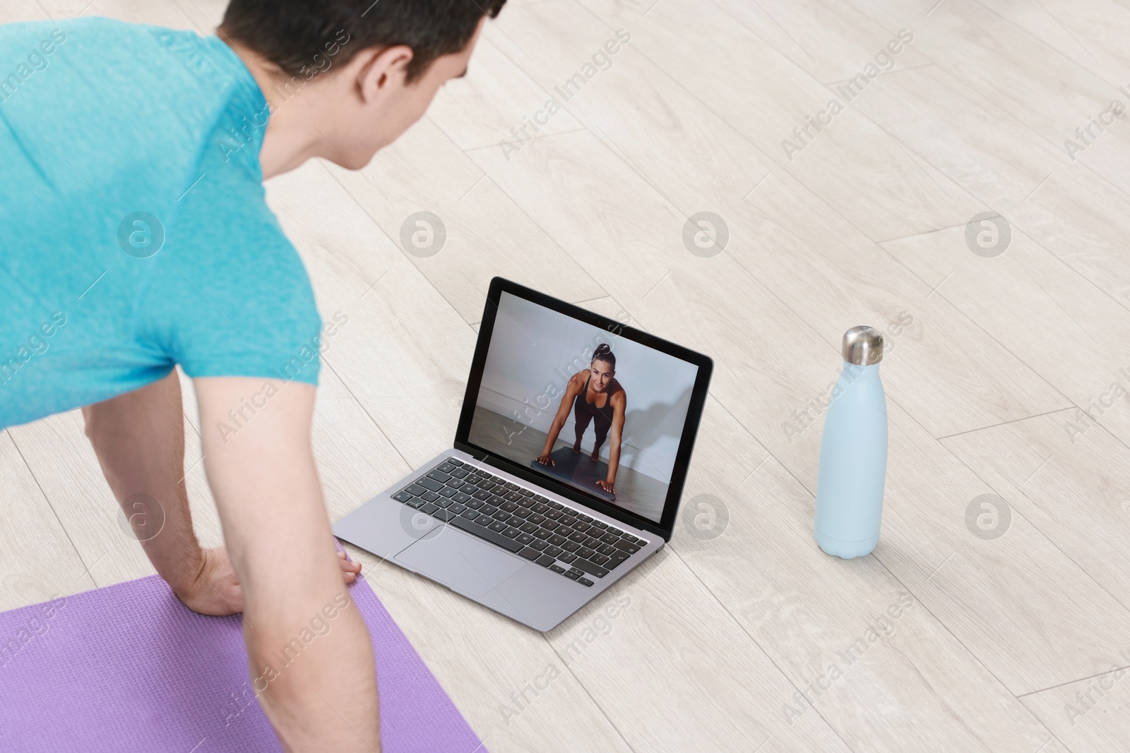 Photo of Online fitness trainer. Man doing exercise near laptop at home