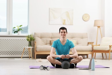 Photo of Online fitness trainer. Happy man with kettlebell near laptop at home