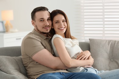 Photo of Man hugging his happy girlfriend on sofa at home