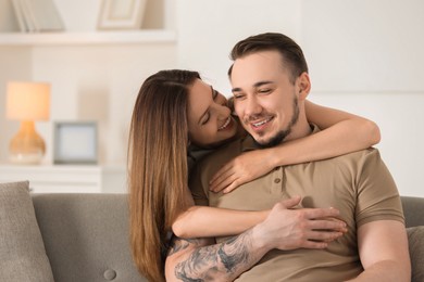 Photo of Woman hugging her happy boyfriend on sofa at home