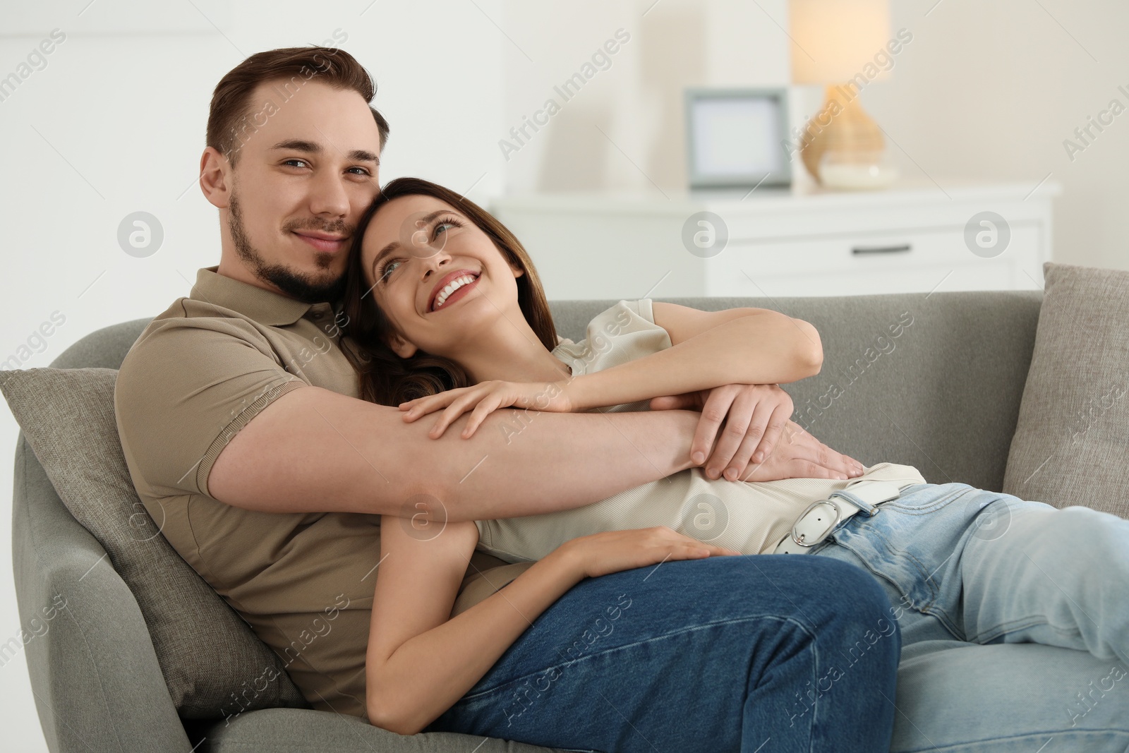 Photo of Man hugging his happy girlfriend on sofa at home