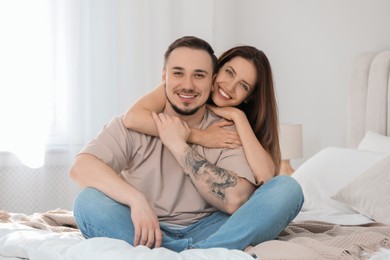 Photo of Happy couple sitting on bed and hugging at home