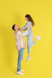 Photo of Happy man lifting his girlfriend on yellow background