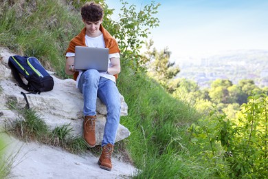 Travel blogger using laptop on stone outdoors, space for text