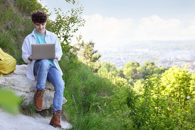 Travel blogger using laptop on stone outdoors, space for text