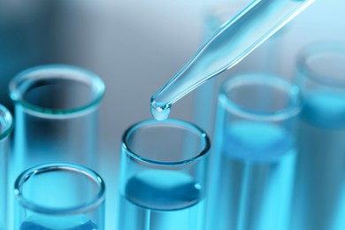 Dripping liquid from pipette into test tube on blurred background, closeup