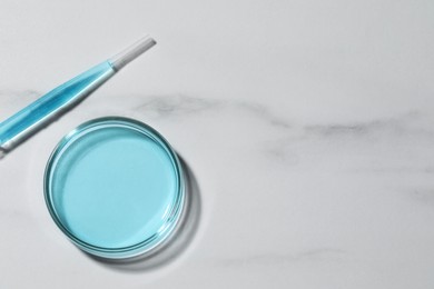 Pipette and petri dish with liquid on white marble table, flat lay. Space for text