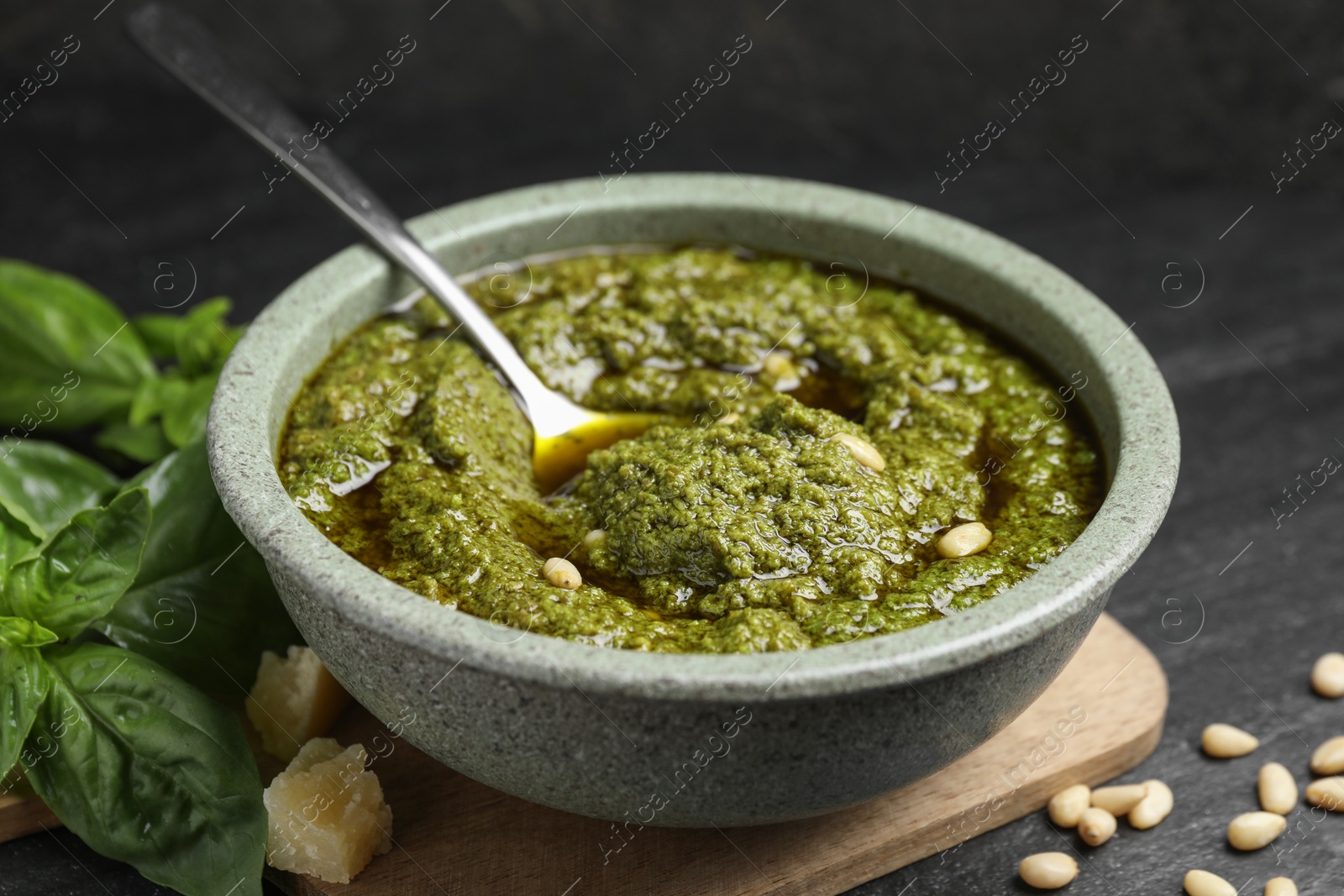 Photo of Tasty pesto sauce in bowl, pine nuts, cheese and basil on black table, closeup