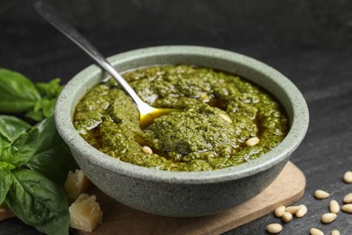 Photo of Tasty pesto sauce in bowl, pine nuts, cheese and basil on black table, closeup