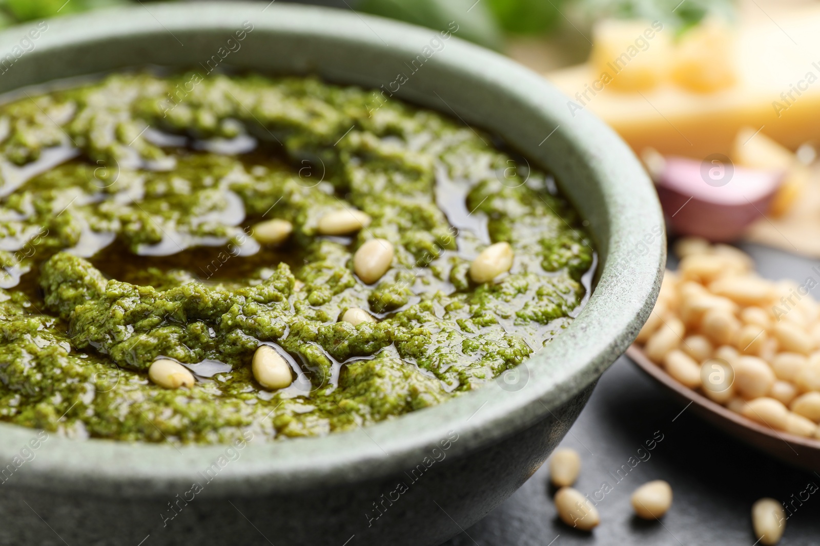 Photo of Tasty pesto sauce in bowl and pine nuts on table, closeup