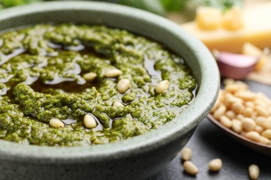 Tasty pesto sauce in bowl and pine nuts on table, closeup