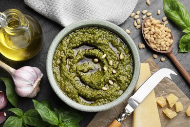 Photo of Tasty pesto sauce in bowl, basil, pine nuts, cheese, garlic and oil on black table, flat lay