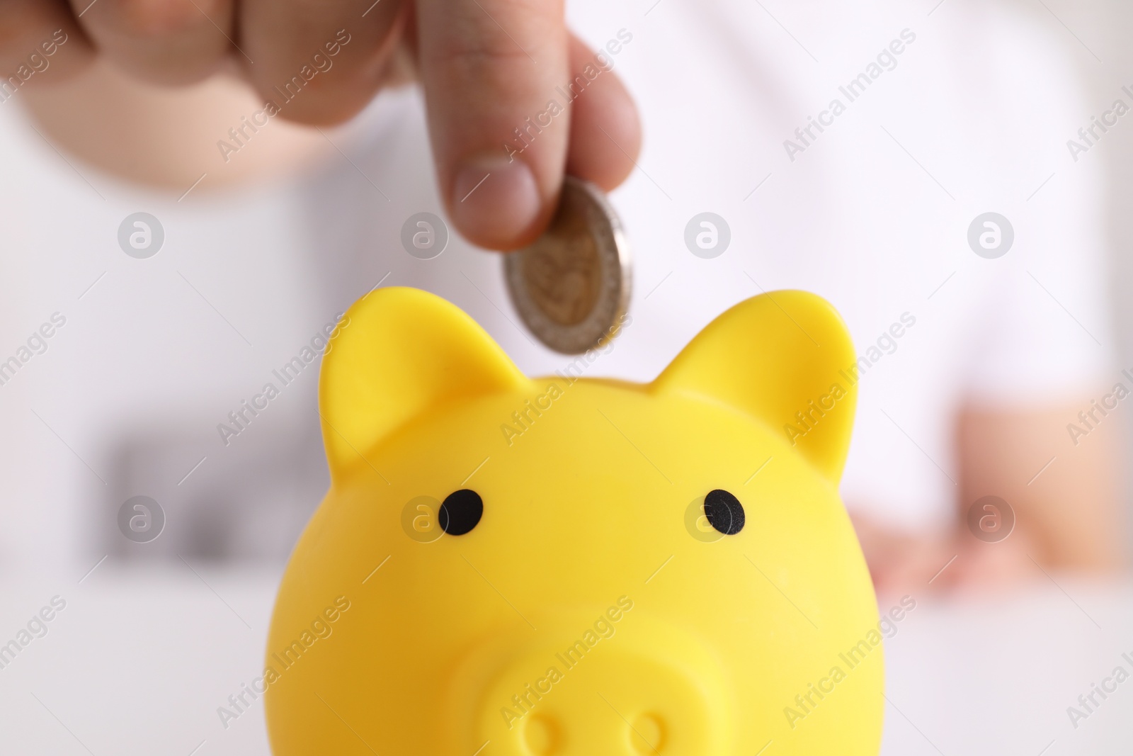 Photo of Man putting coin into yellow piggy bank at table, closeup