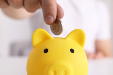 Photo of Man putting coin into yellow piggy bank at table, closeup