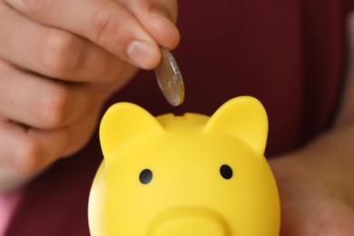 Photo of Man putting coin into piggy bank on yellow background, closeup