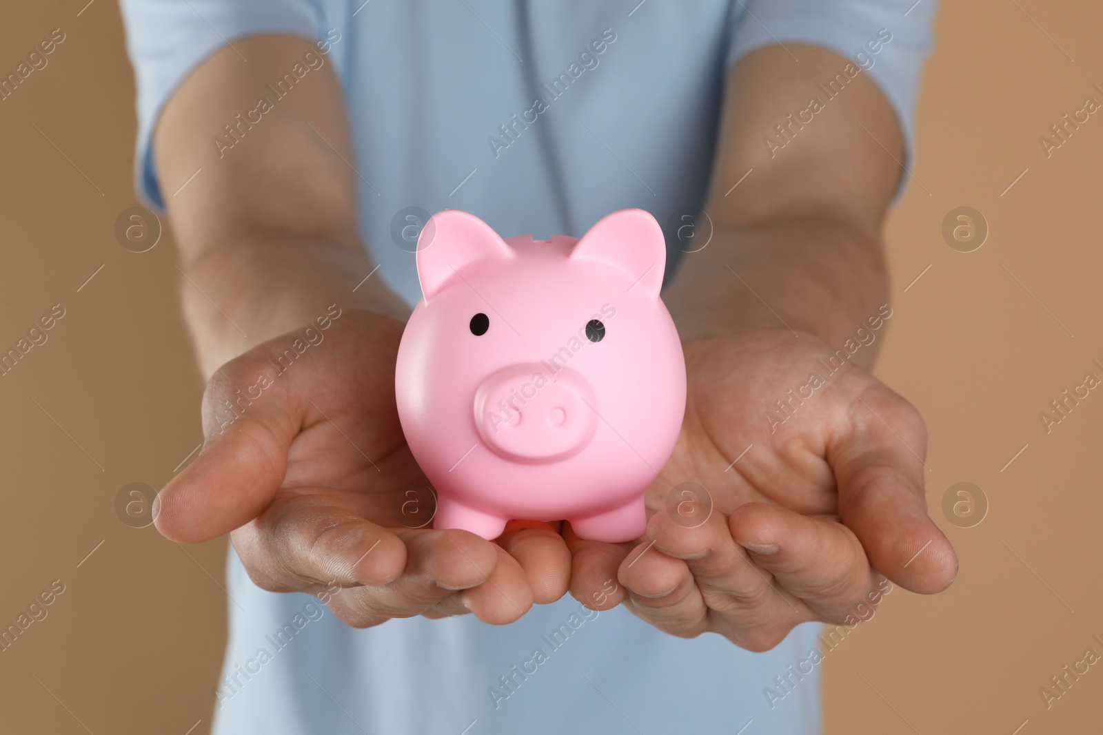 Photo of Man with pink piggy bank on light brown background, closeup