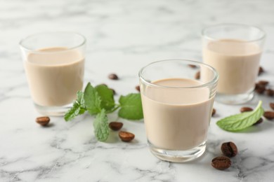 Coffee cream liqueur in glasses, mint and beans on white marble table