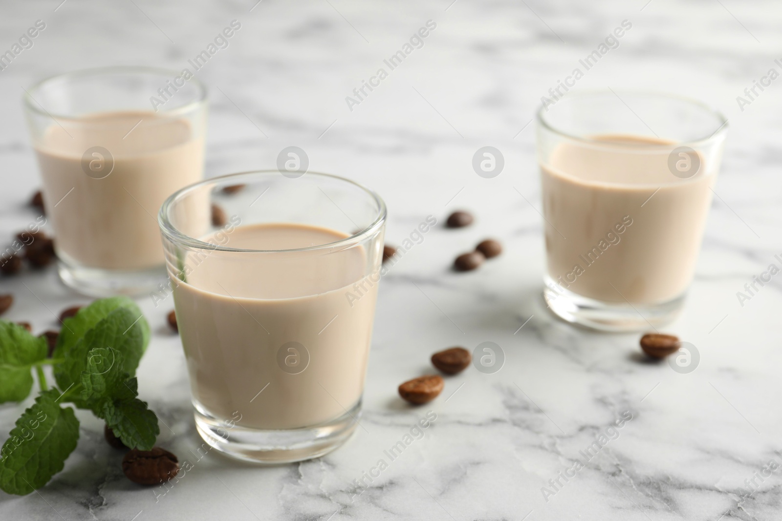 Photo of Coffee cream liqueur in glasses, mint and beans on white marble table