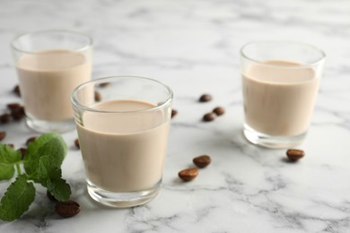 Photo of Coffee cream liqueur in glasses, mint and beans on white marble table