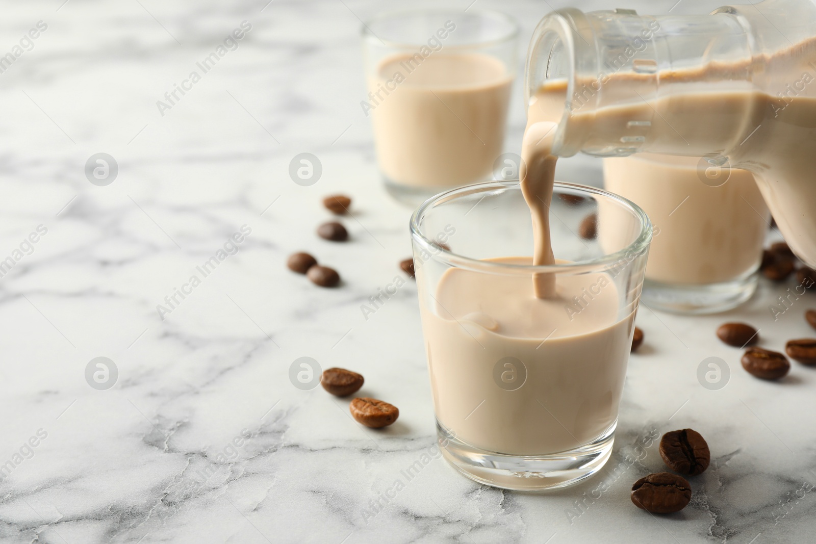 Photo of Pouring coffee cream liqueur into glass at white marble table, closeup. Space for text