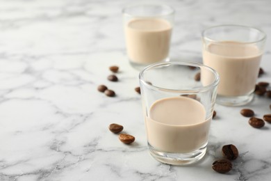 Photo of Coffee cream liqueur in glasses and beans on white marble table, space for text