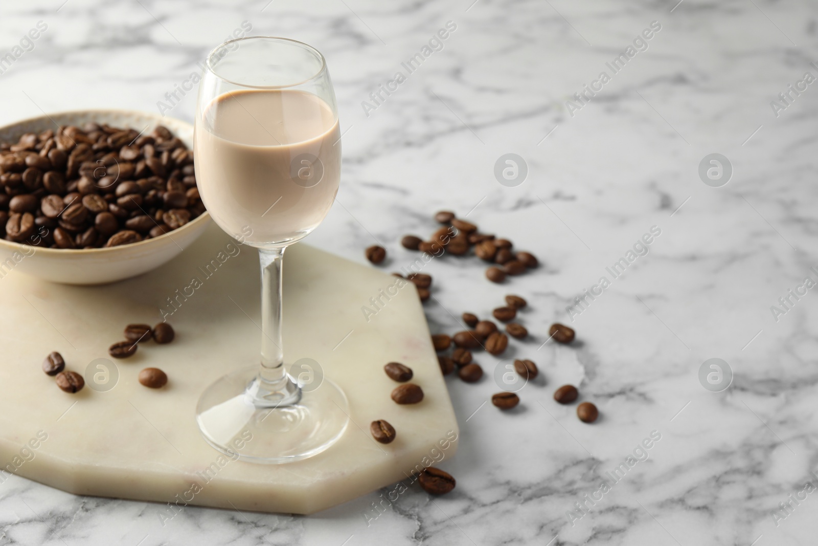 Photo of Coffee cream liqueur in glass and beans on white marble table, space for text