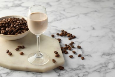 Coffee cream liqueur in glass and beans on white marble table, space for text