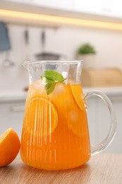 Freshly made lemonade in jug, mint and orange on wooden table in kitchen