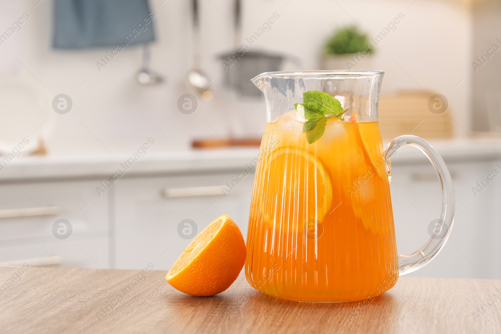 Photo of Freshly made lemonade in jug, mint and orange on wooden table in kitchen, space for text