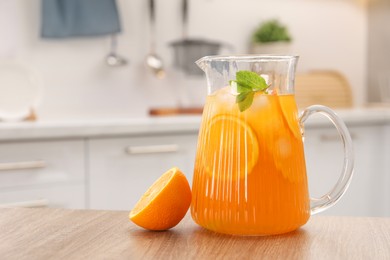 Photo of Freshly made lemonade in jug, mint and orange on wooden table in kitchen, space for text