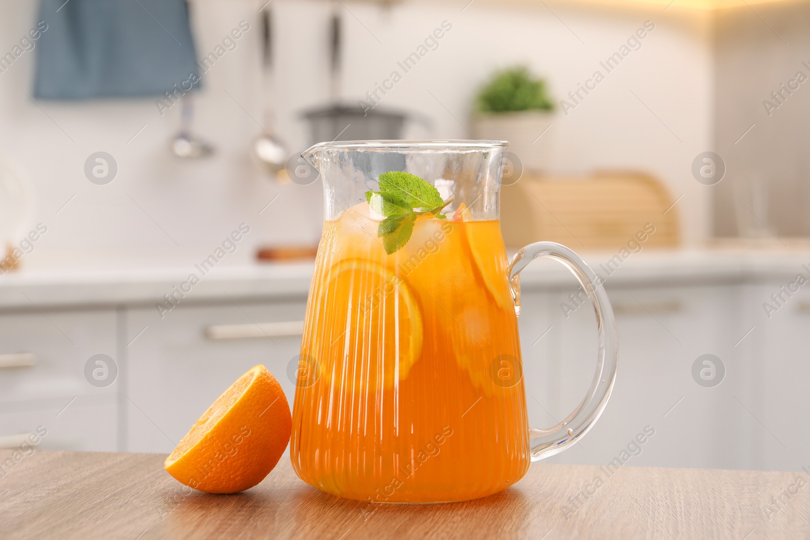 Photo of Freshly made lemonade in jug, mint and orange on wooden table in kitchen