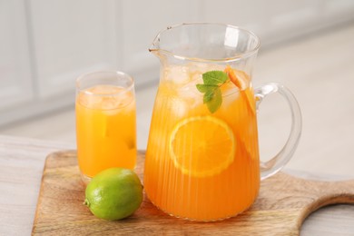 Photo of Tasty lemonade with orange in jug, glass and lime on wooden table in kitchen