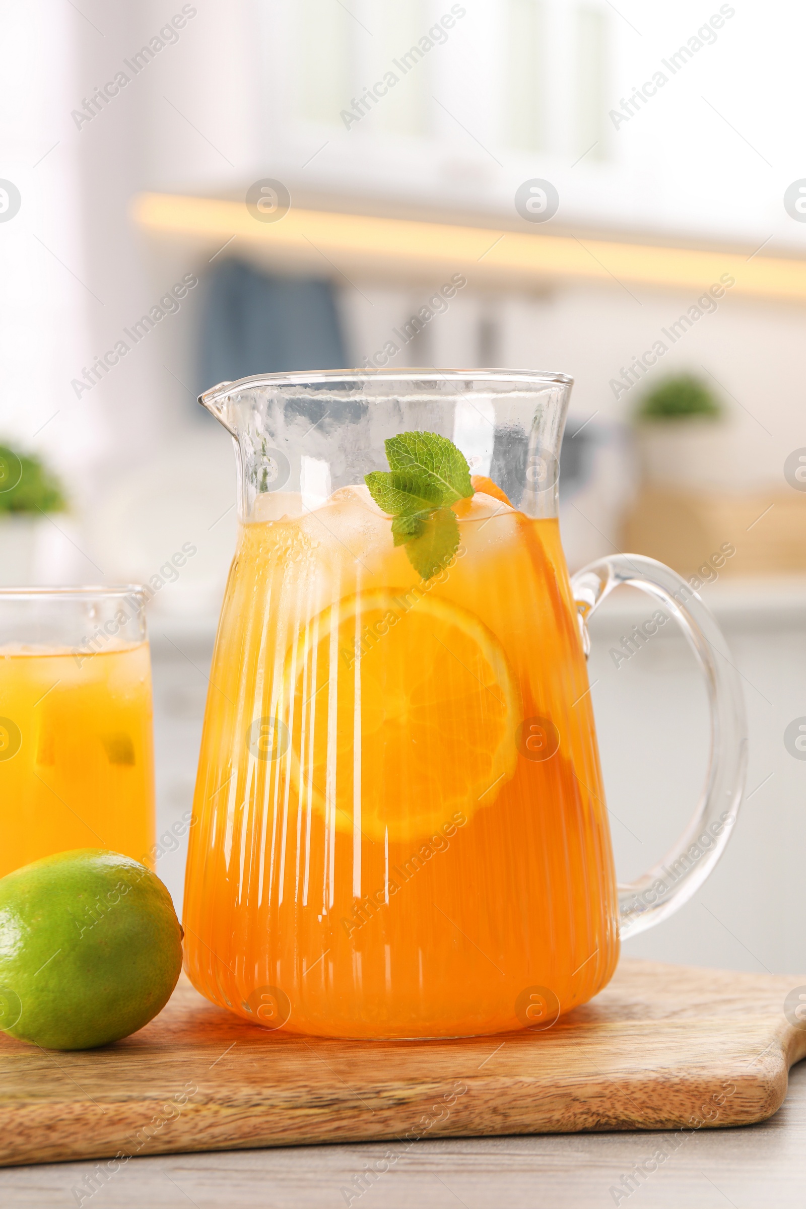 Photo of Tasty lemonade with orange in jug, glass and lime on wooden table in kitchen