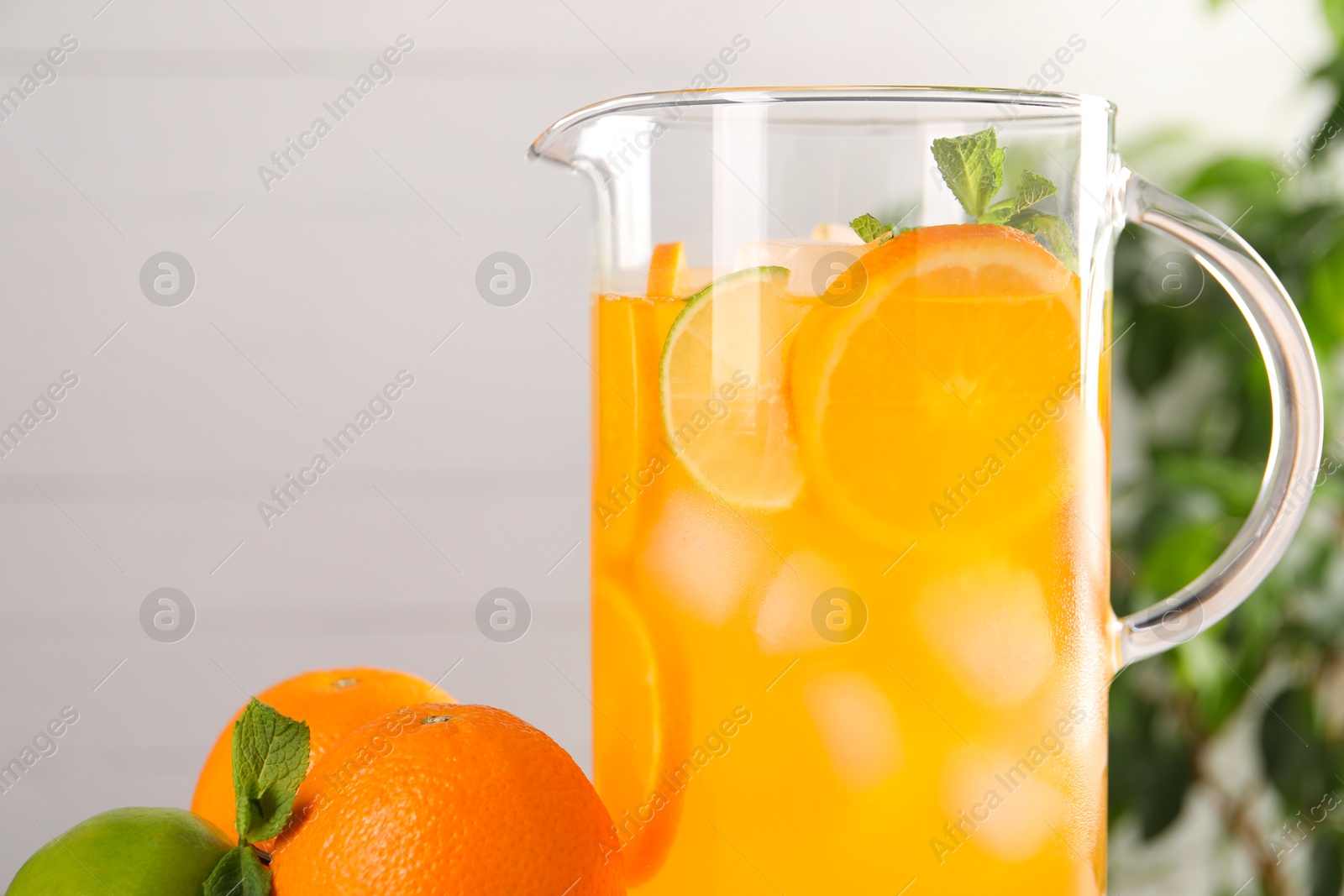 Photo of Freshly made lemonade in jug and citrus fruits against blurred background