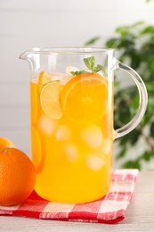 Freshly made lemonade in jug and orange on light wooden table