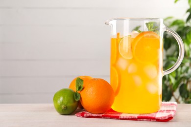 Photo of Freshly made lemonade in jug and citrus fruits on light wooden table, space for text