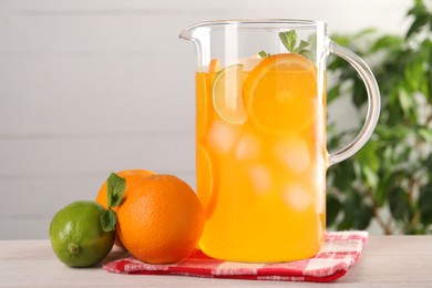 Freshly made lemonade in jug and citrus fruits on light wooden table