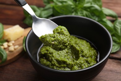 Photo of Taking tasty pesto sauce at wooden table, closeup