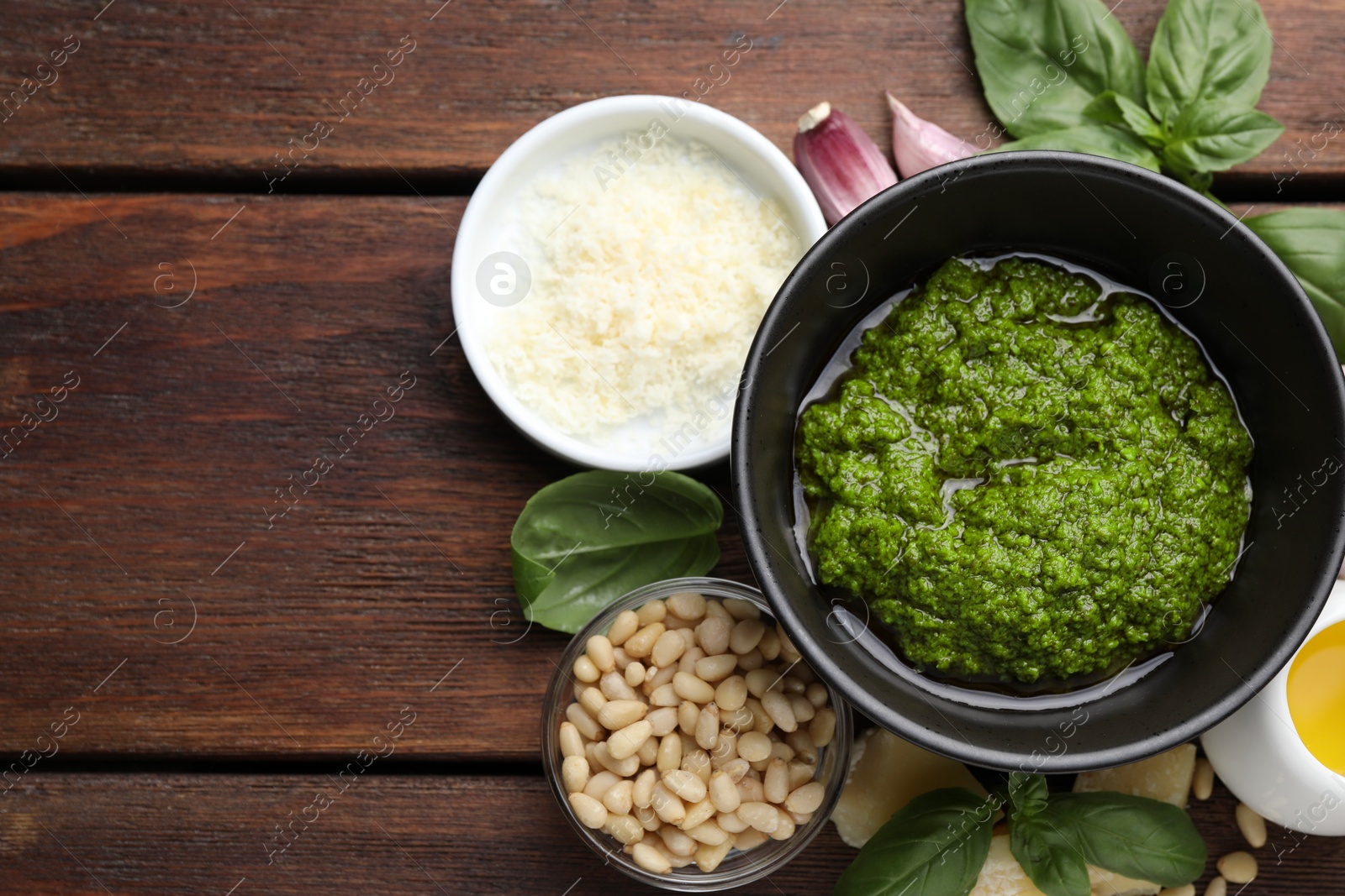 Photo of Tasty pesto sauce in bowl, basil, pine nuts, cheese, garlic on wooden table, top view. Space for text