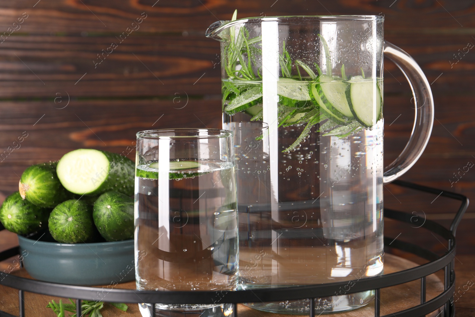 Photo of Tray with refreshing cucumber water with rosemary and vegetable on wooden table