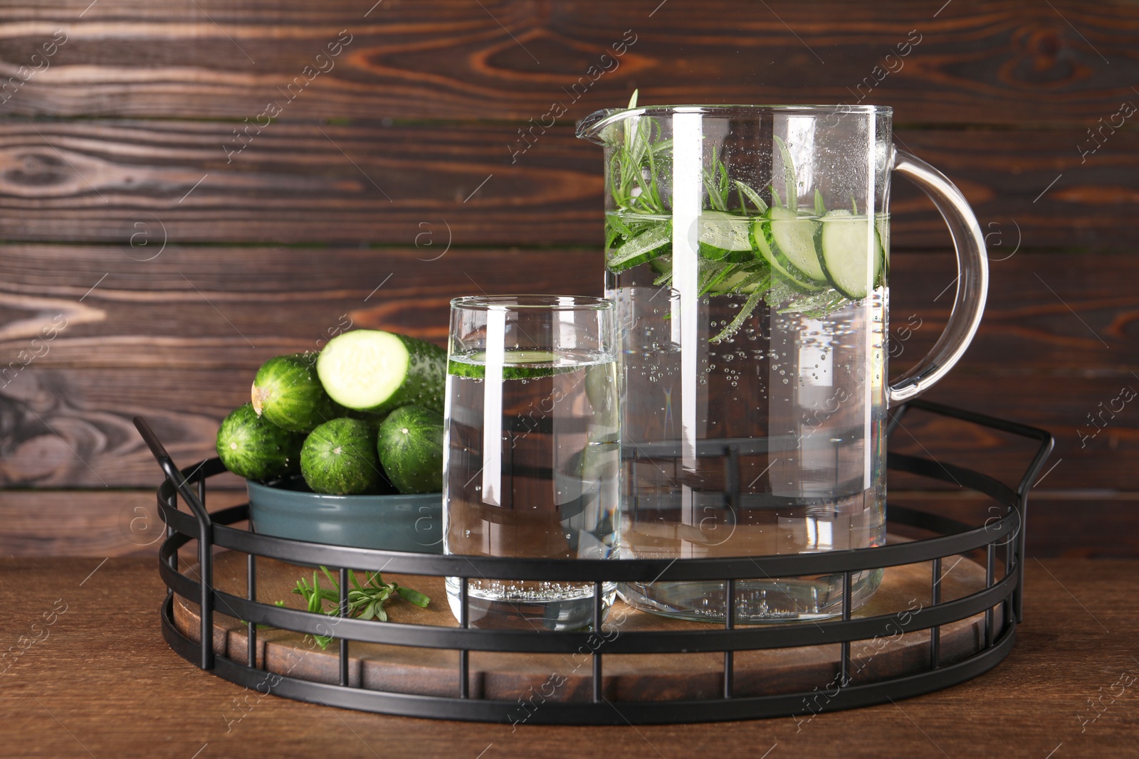 Photo of Tray with refreshing cucumber water with rosemary and vegetable on wooden table