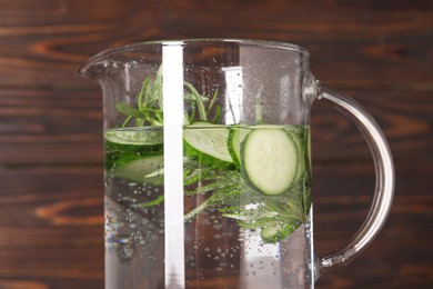 Photo of Refreshing cucumber water with rosemary in jug on wooden background, closeup