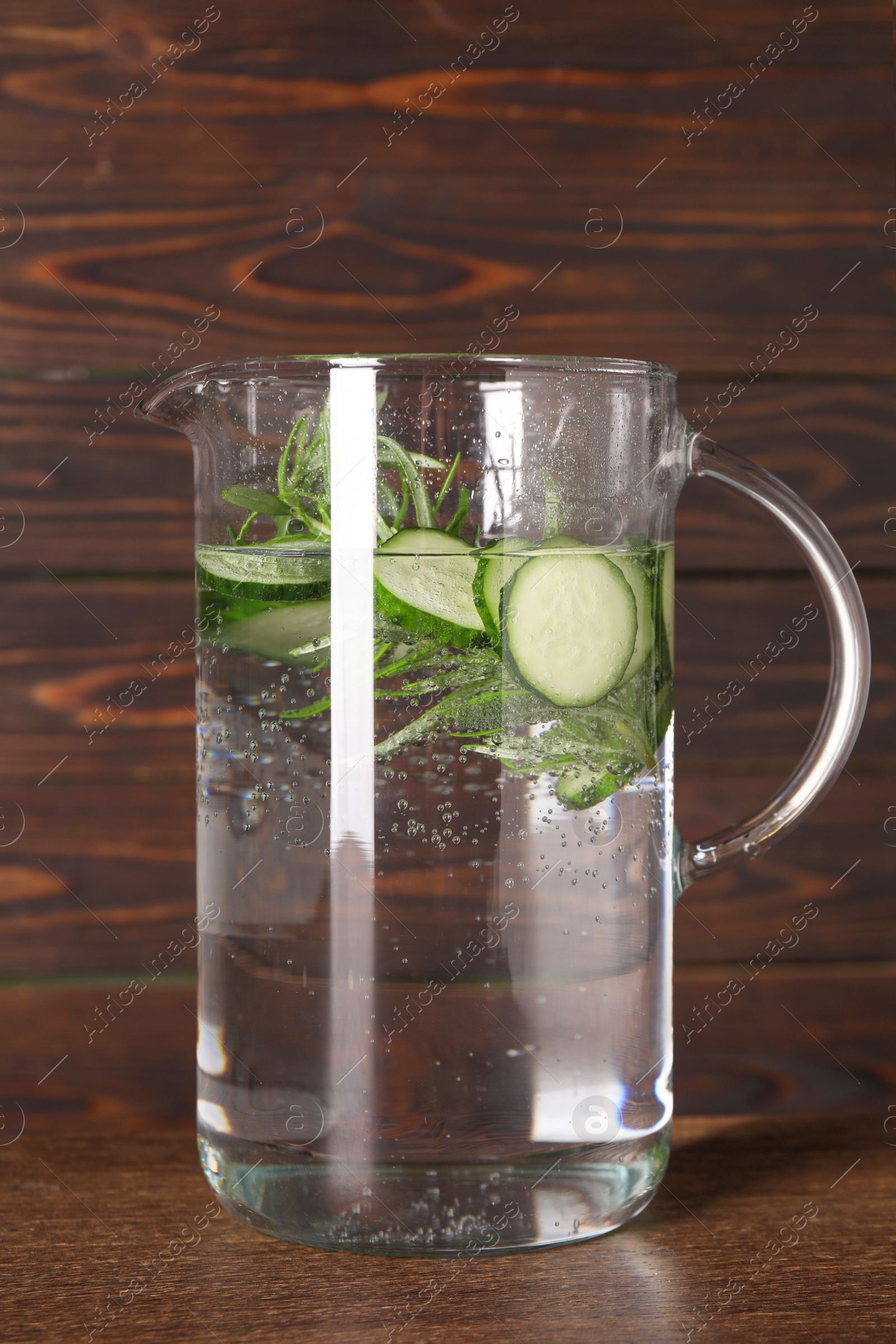 Photo of Refreshing cucumber water with rosemary in jug on wooden table